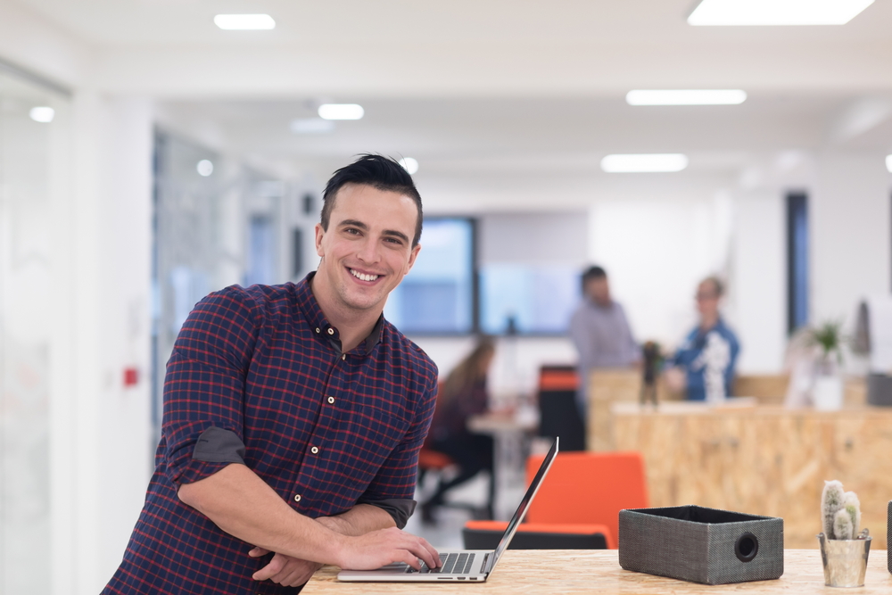 Man leaning on desk in office with hand on laptop