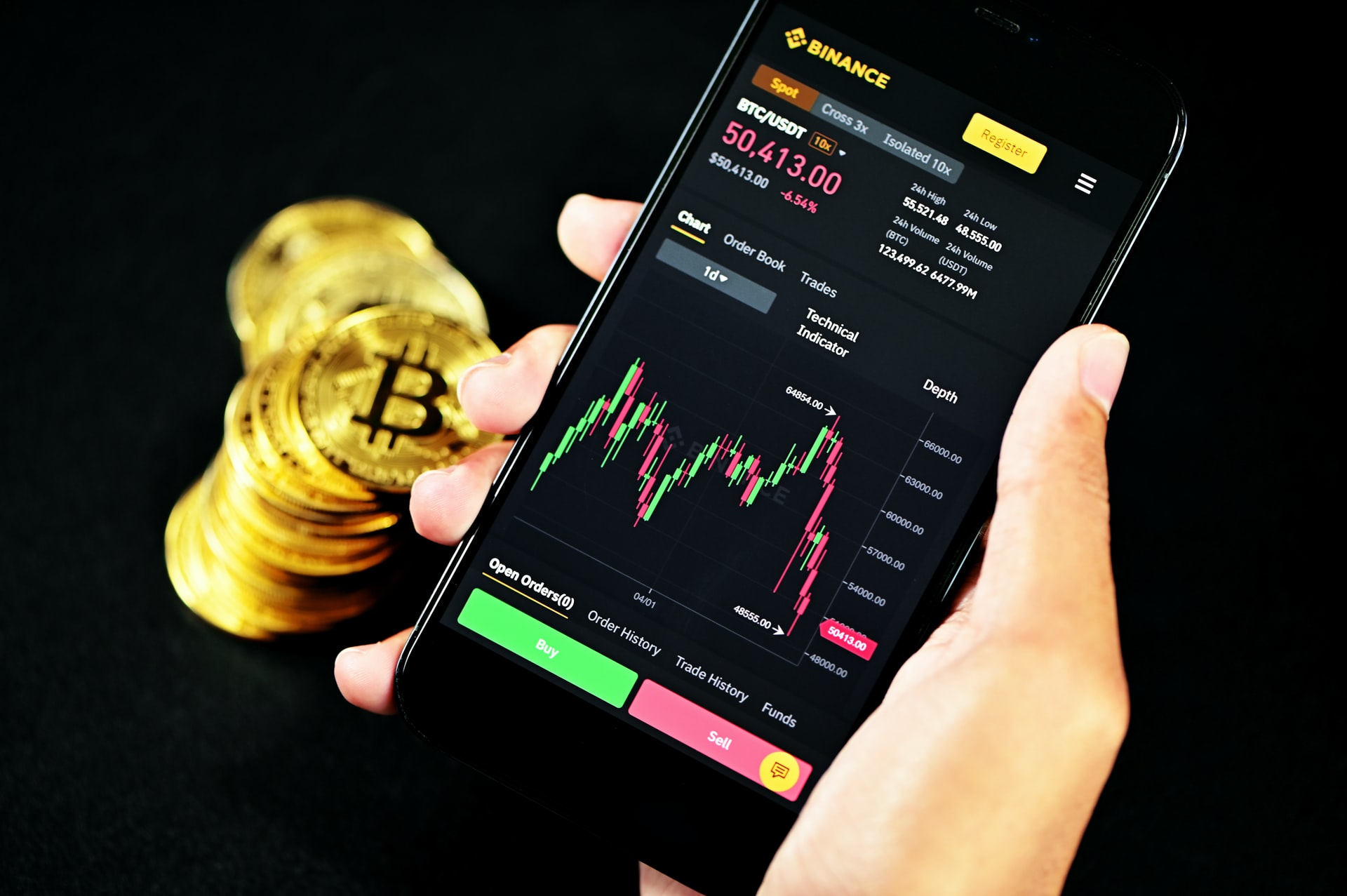 stack of bitcoin and a mobile phone showing cryptocurrency investing on the Binance app